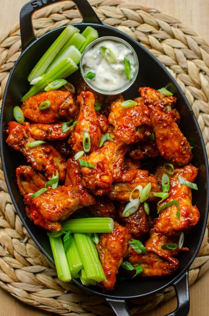 Buffalo wings in a black baking dish with celery, green onions, and dip.