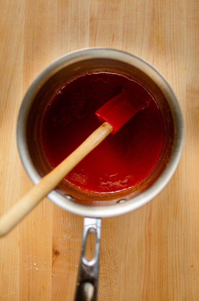 Sauce in a pot being stirred with a wooden spatula.
