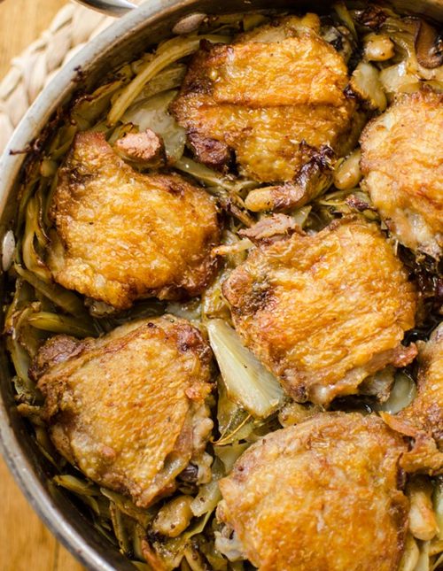 Crispy braised chicken thighs in a pot with mushrooms, white beans, cabbage and bacon