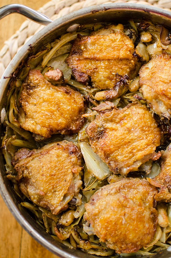 Crispy braised chicken thighs in a pot with mushrooms, white beans, cabbage and bacon