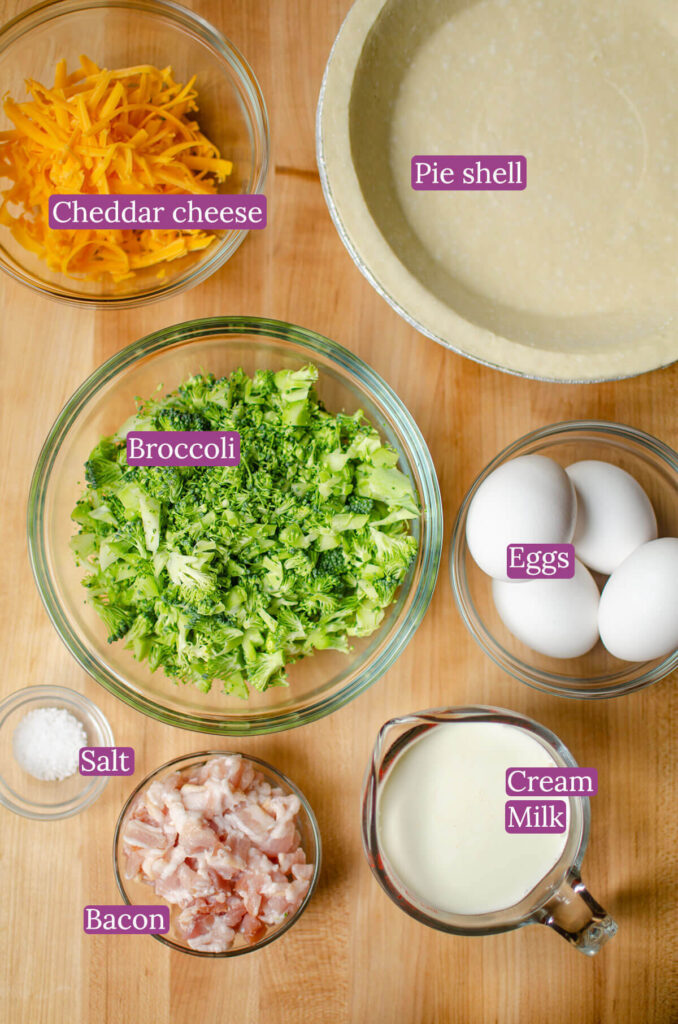 Ingredients for quiche in glass bowls on a wooden board.
