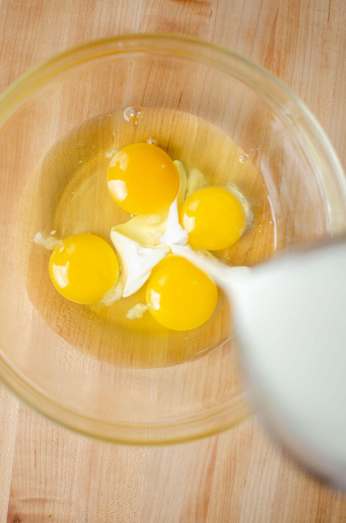 Cream and milk being pour into a bowl with four eggs.