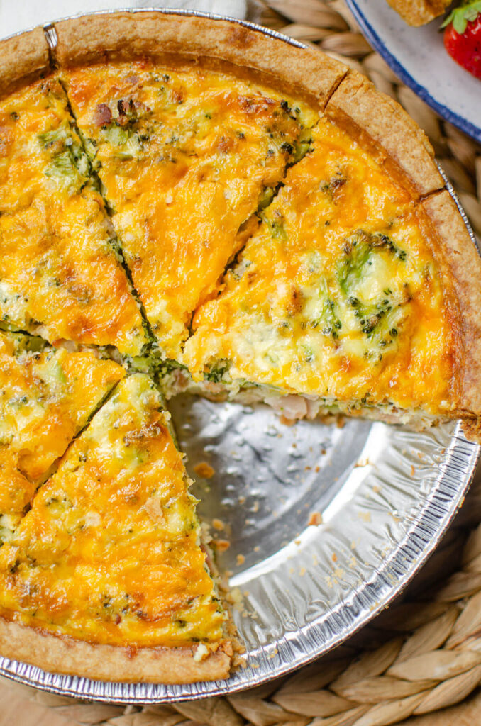 Closeup of quiche in a pie plate with a piece missing.