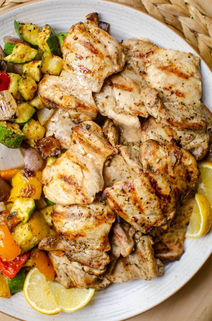 A platter of grilled chicken thighs with grilled vegetables.