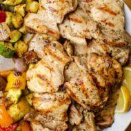 Closeup of grilled greek chicken with vegetables on a platter.