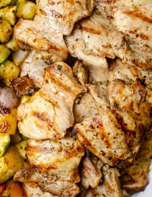 Closeup of grilled greek chicken with vegetables on a platter.