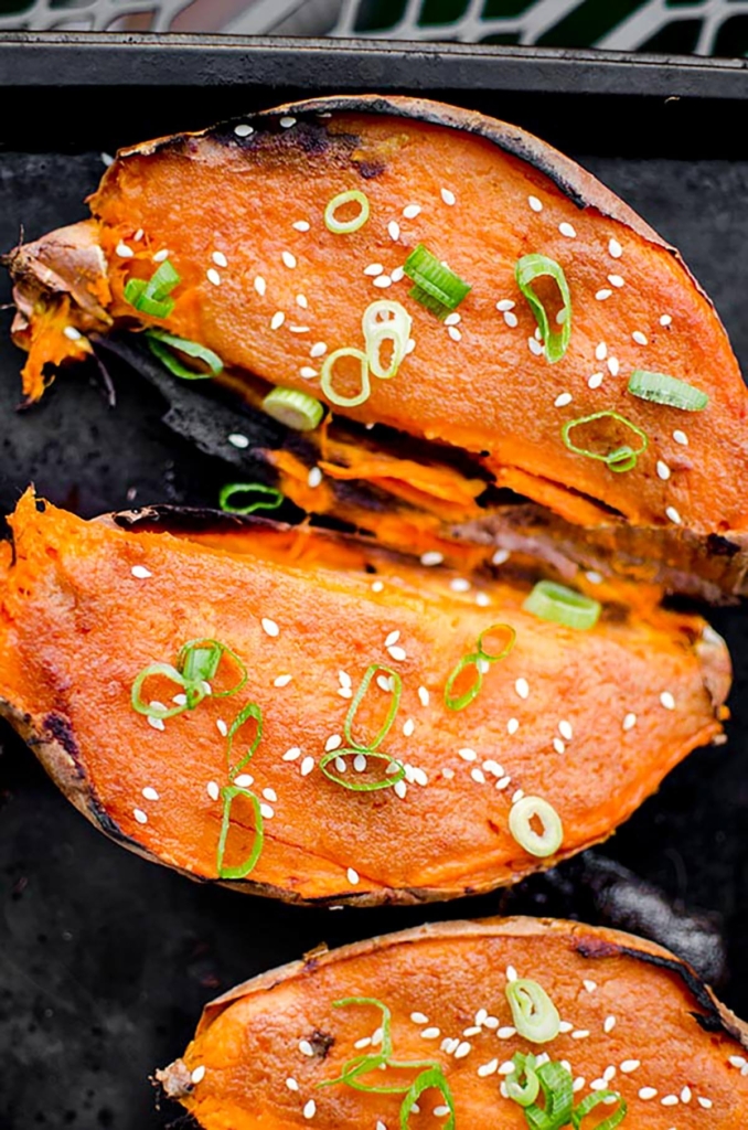 Cooked sweet potatoes on a baking sheet with scallions and sesame seeds