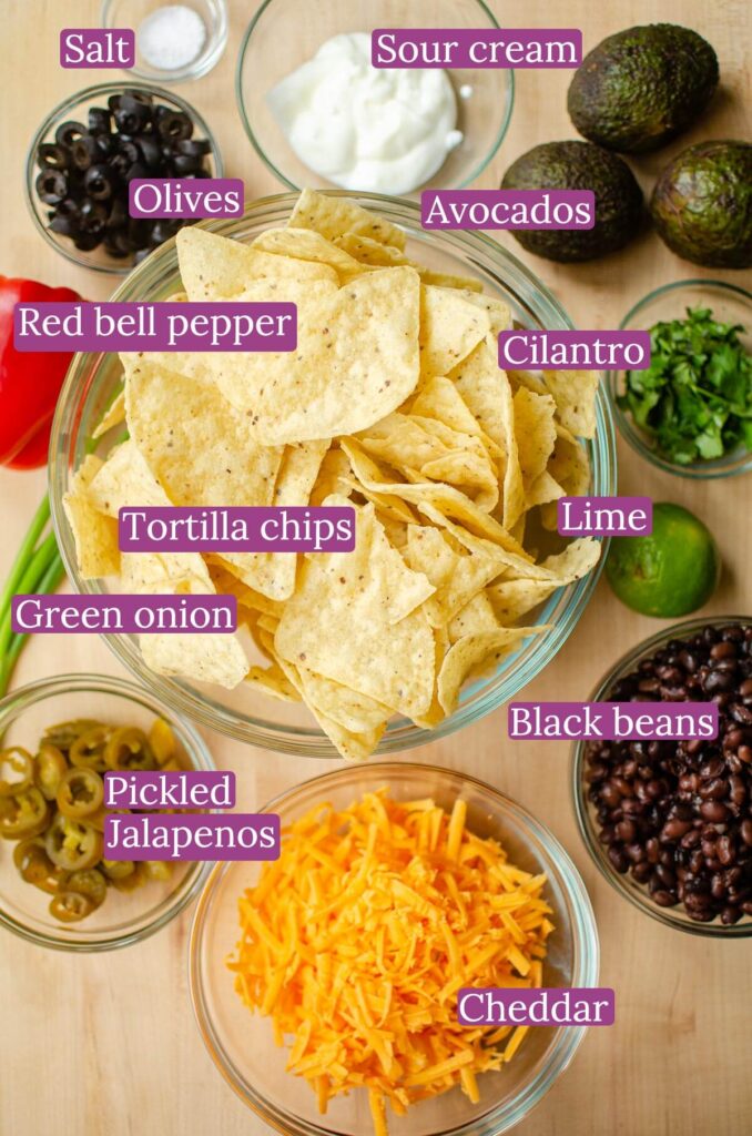 Ingredients for nachos on a wooden cutting board.