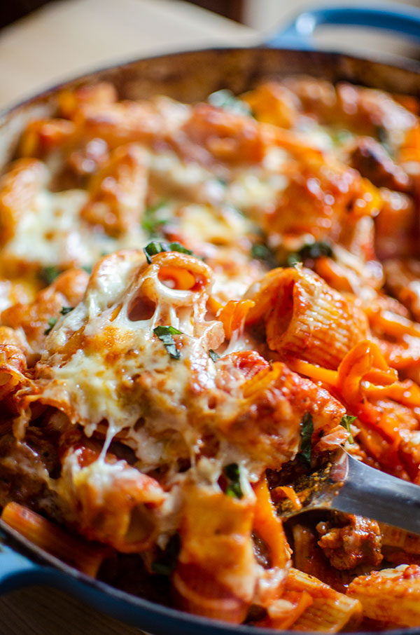 A closeup of a scoop being spooned out of cheesy baked pasta