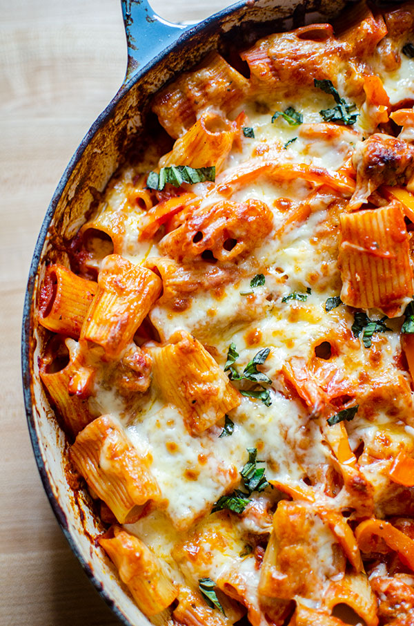 Sausage and pepper pasta in a blue Le Creuset braising dish with melted cheese and fresh basil on top.