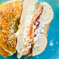 Closeup of half a bagel with scallion cream cheese, lox and red onions on a blue plate.