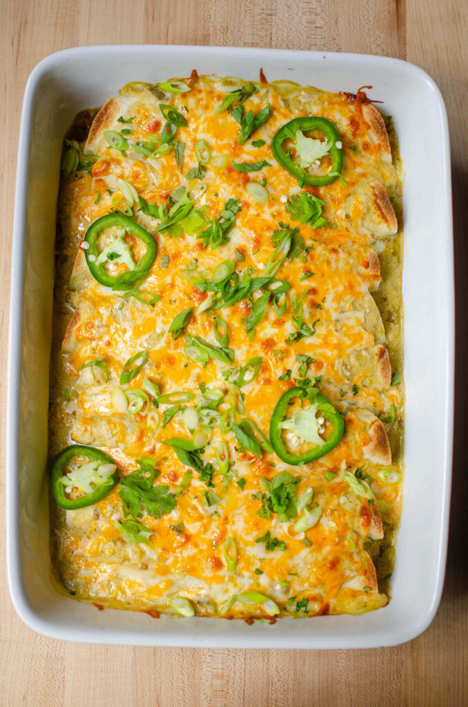 A pan of baked enchiladas with slices of jalapeno and cilantro sprinkled on top.