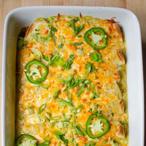 A closeup of half a pan of baked enchiladas with slices of jalapeno and cilantro sprinkled on top.