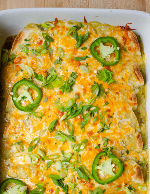 A closeup of half a pan of baked enchiladas with slices of jalapeno and cilantro sprinkled on top.
