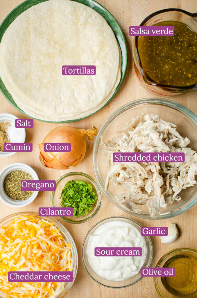 Ingredients for enchiladas in glass bowls on a wooden board.