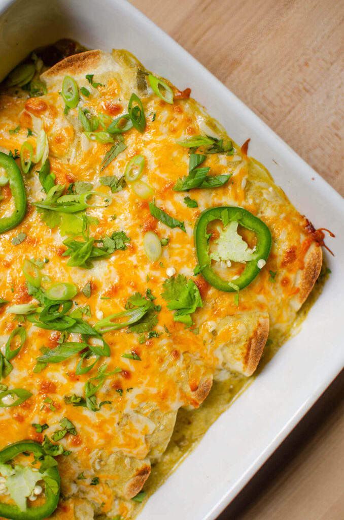 Cooked enchiladas smothered with melted cheese, cilantro and jalapeno in a white cassrole dish.