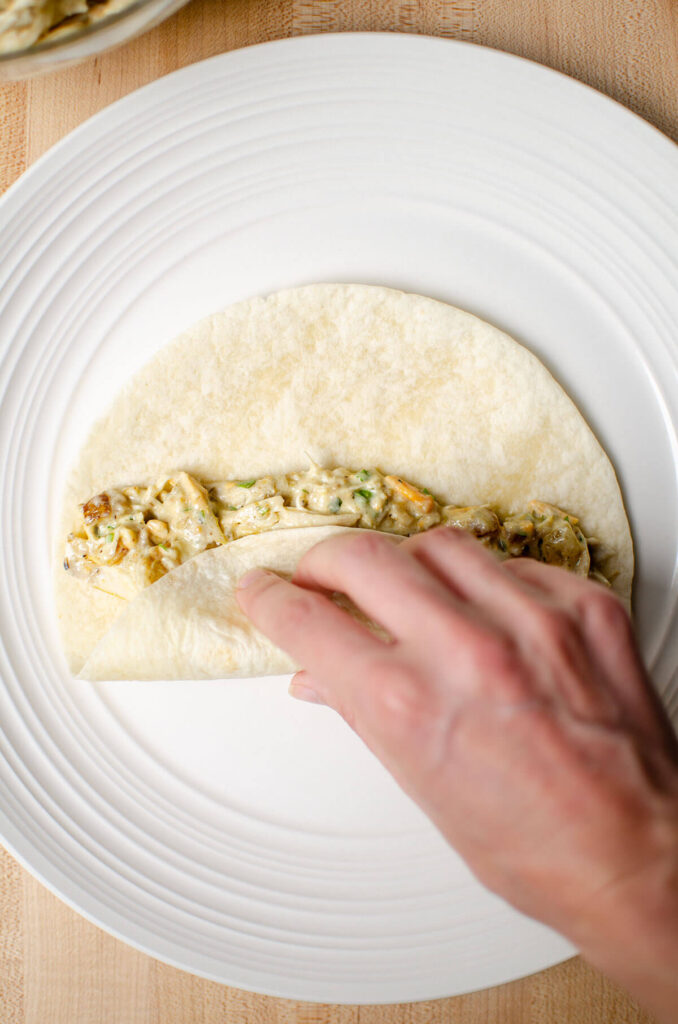 A plate with a tortilla and filling being rolled up.
