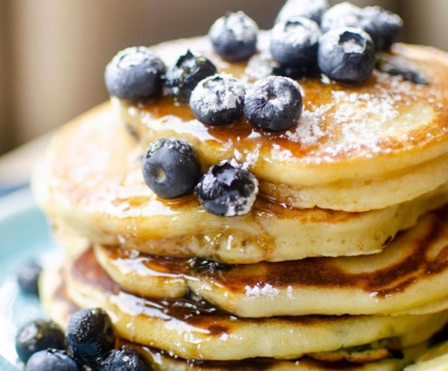 Closeup of a stack of pancakes with fresh bluberries, maple syrup and icing sugar on a blue plate