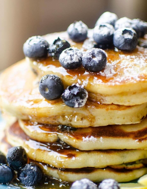 Closeup of a stack of pancakes with fresh bluberries, maple syrup and icing sugar on a blue plate