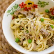 Braised lamb ragu with peas tossed with pasta in a bowl.