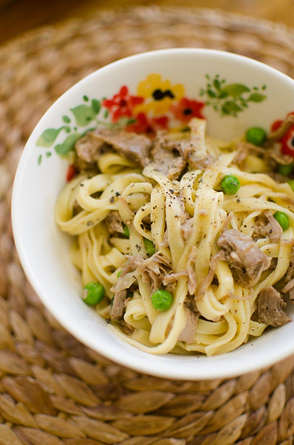 Braised lamb ragu with peas tossed with pasta in a bowl.