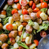 Closeup on sheet pan oven baked gnocchi with sausage and vegetables on a baking sheet with a spoon.