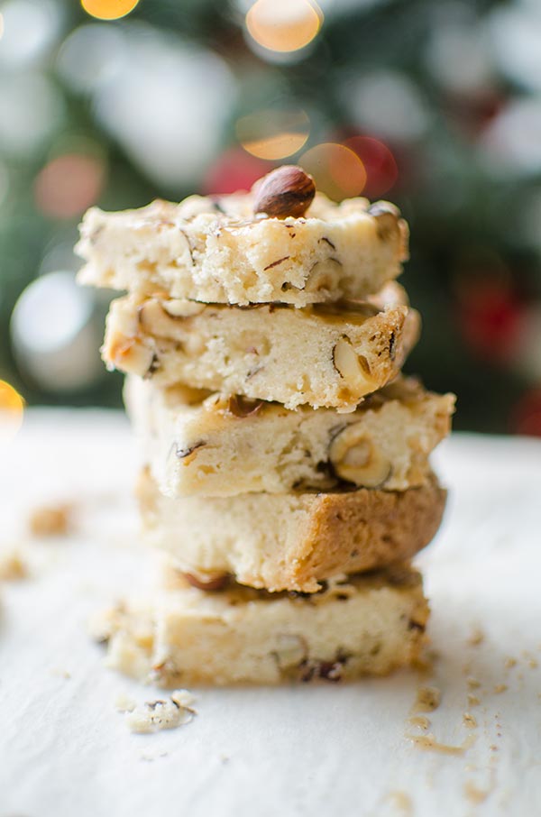 Hazelnut shortbread bars with a chai glaze stacked on top of each other on a plate with a Christmas tree in the background