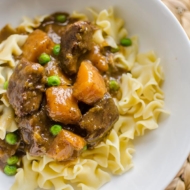 Beef and butternut squash stew on egg noodles in a white bowl.