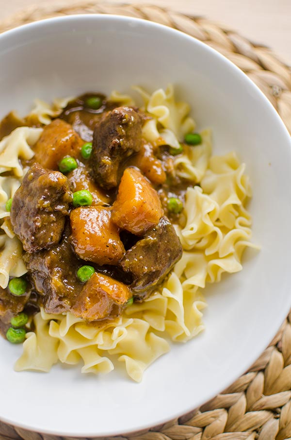 Beef and butternut squash stew on egg noodles in a white bowl.