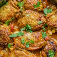 Braised chicken thighs with white beans in a pot with parsley sprinkled on top.