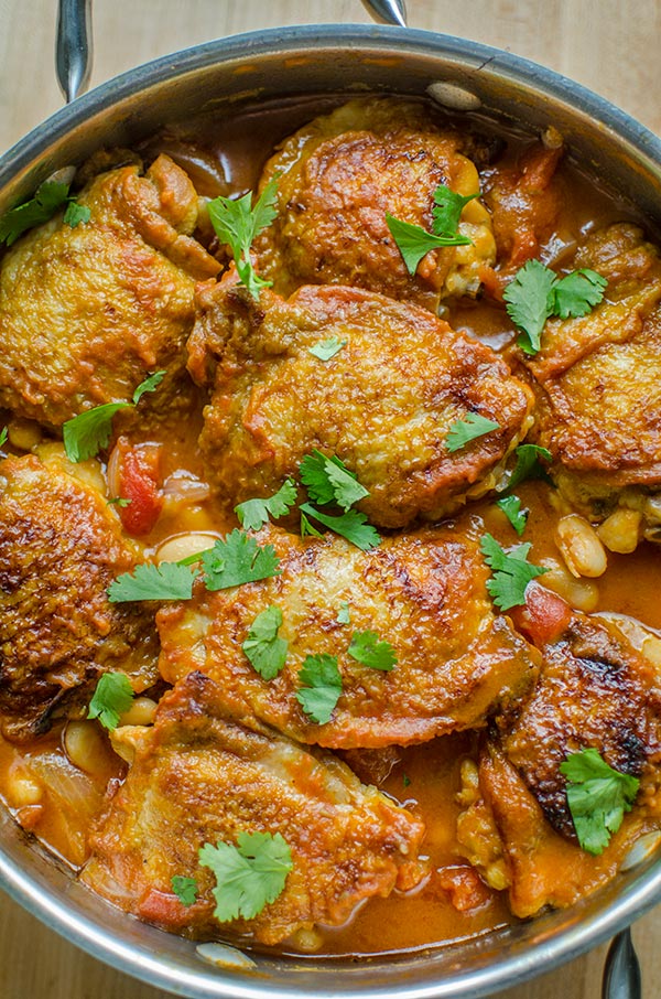 Braised chicken thighs with white beans in a pot with parsley sprinkled on top.