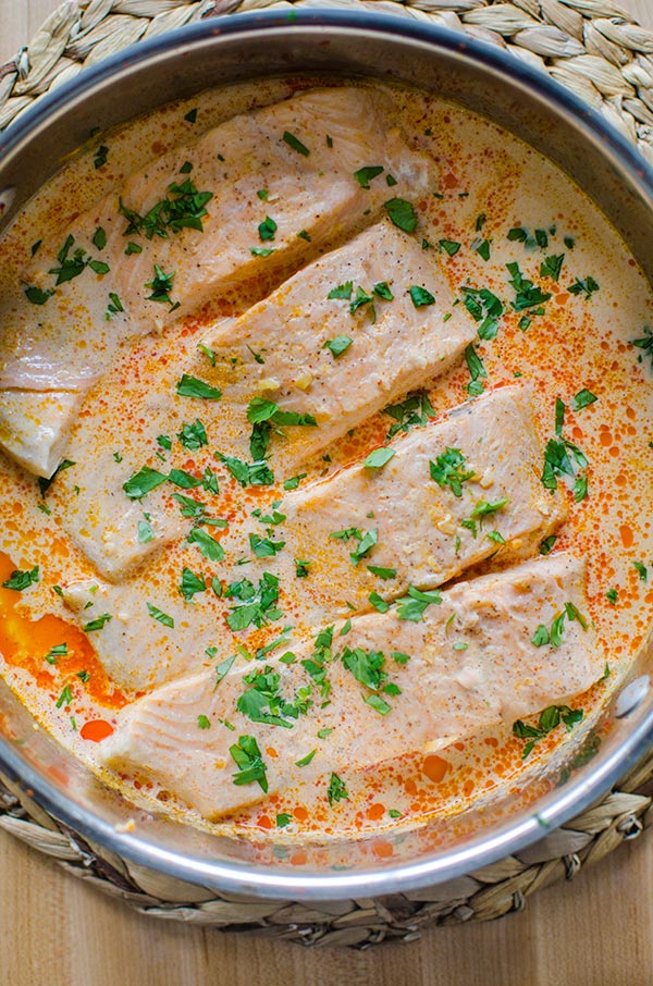 Whole pot of four salmon fillets in their poaching liquid (curried coconut milk) sprinkled with fresh cilantro.