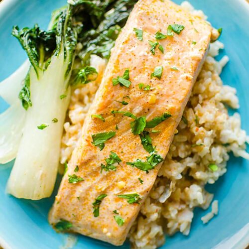 Fillet of salmon overtop brown rice with a side of bok choy on a turquoise plate.