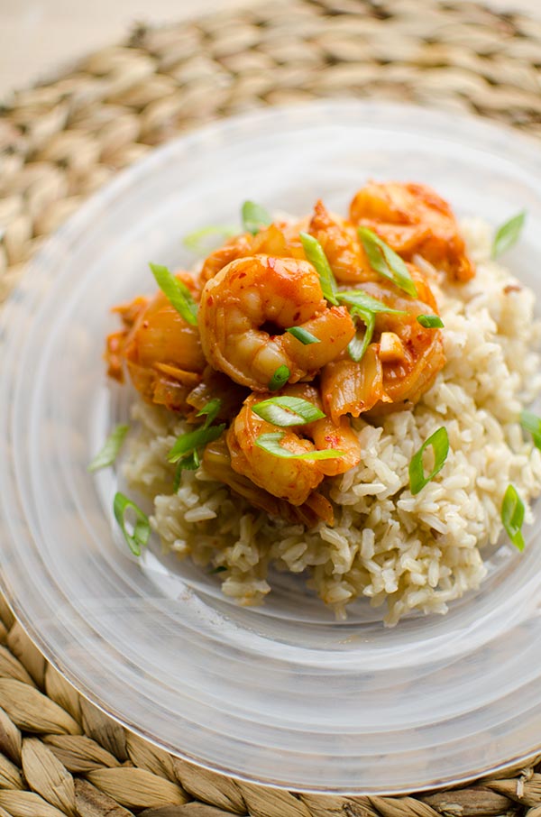 Shrimp and kimchi stir fry over a bed of brown rice with green onions.