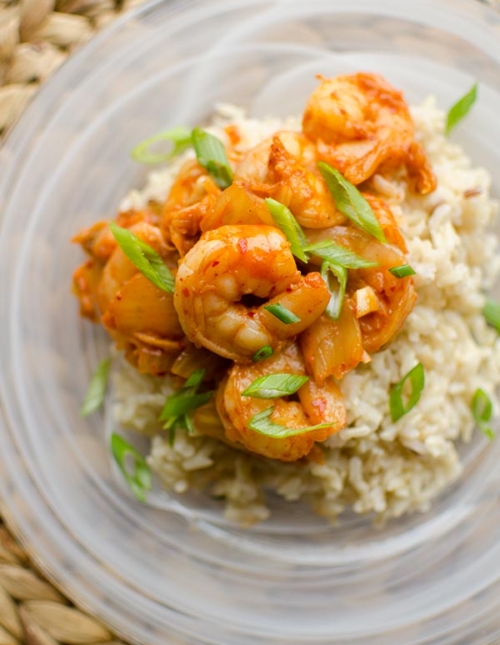 Closeup of shrimp and kimchi stir fry over brown rice with green onions.
