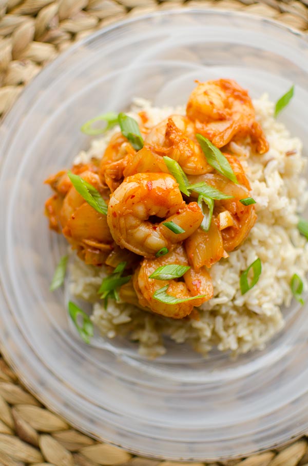Closeup of shrimp and kimchi stir fry over brown rice with green onions.
