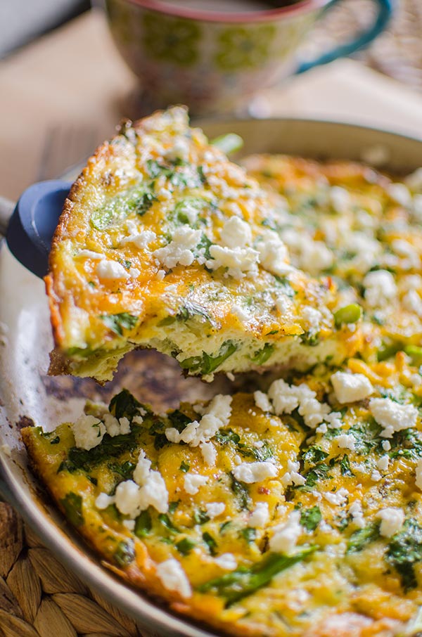 A slice of bacon and asparagus frittata topped with feta.