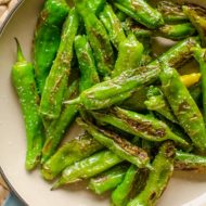 Blistered shishito peppers with salt in a pan.