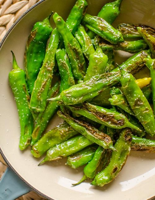 Blistered shishito peppers with salt in a pan.