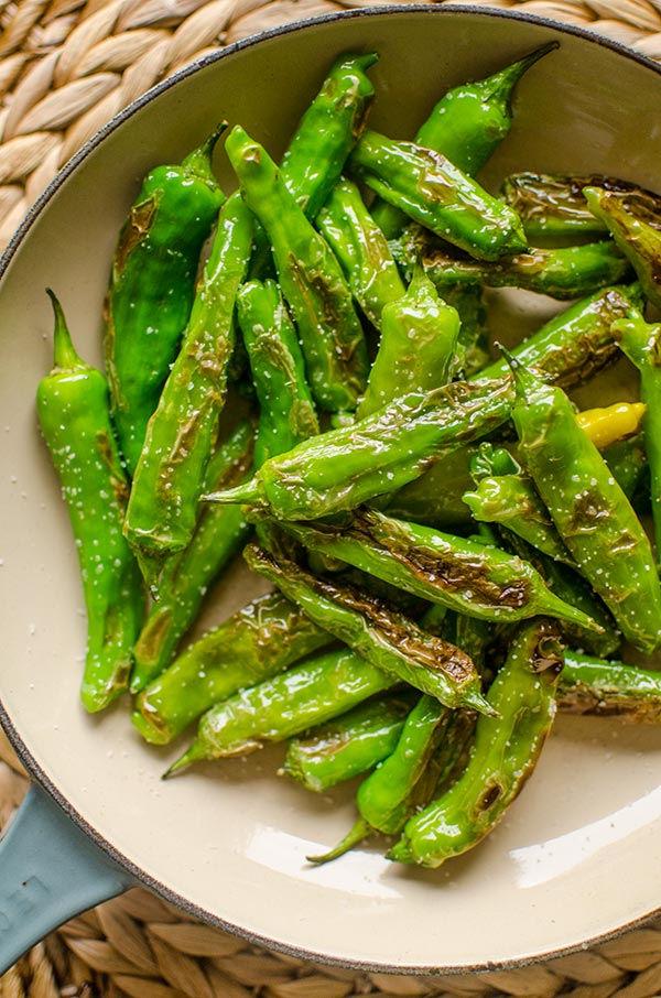 Blistered shishito peppers with salt in a pan.