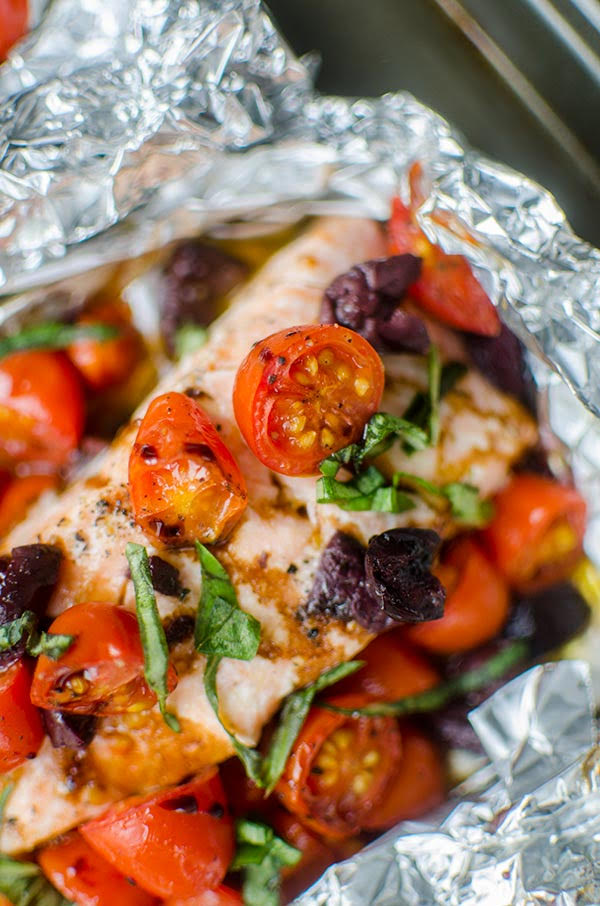 Close up of cherry tomates on top of a grilled salmon fillet, sprinkle with fresh basil, kalamata olives and balsamic glaze.