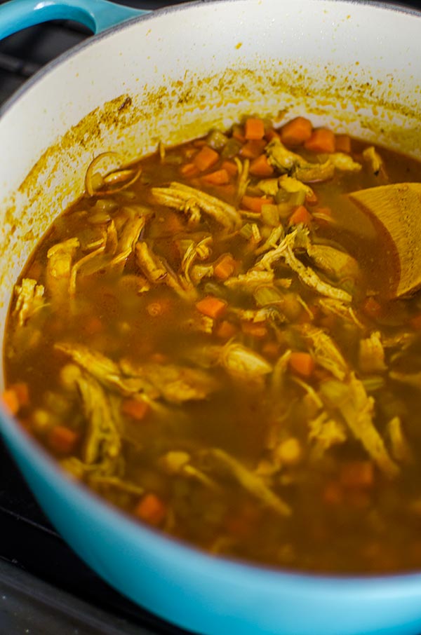 Moroccan chicken soup in a blue Le Creuset pot with a wooden spoon.