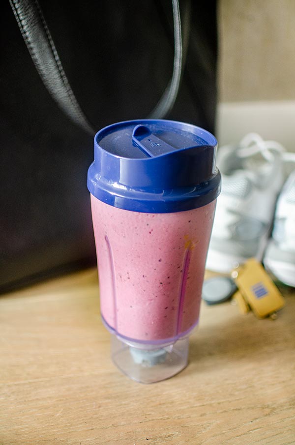 Triple berry smoothie in a to-go cup next to running shoes, keys and a purse.