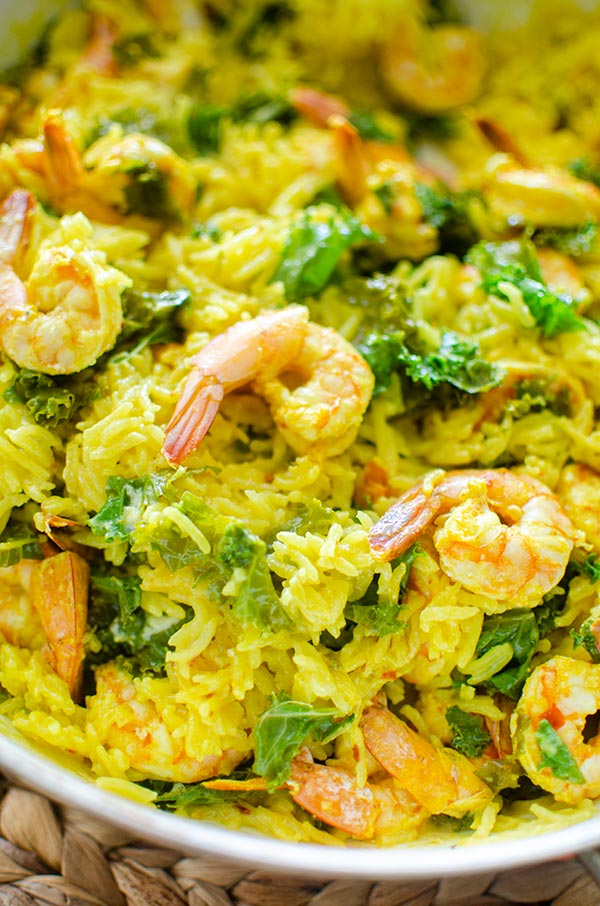 Closeup of coconut turmeric rice with shrimp and thinly sliced kale.