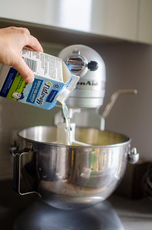 Liquid egg whites being poured into cookie dough in a stand mixer