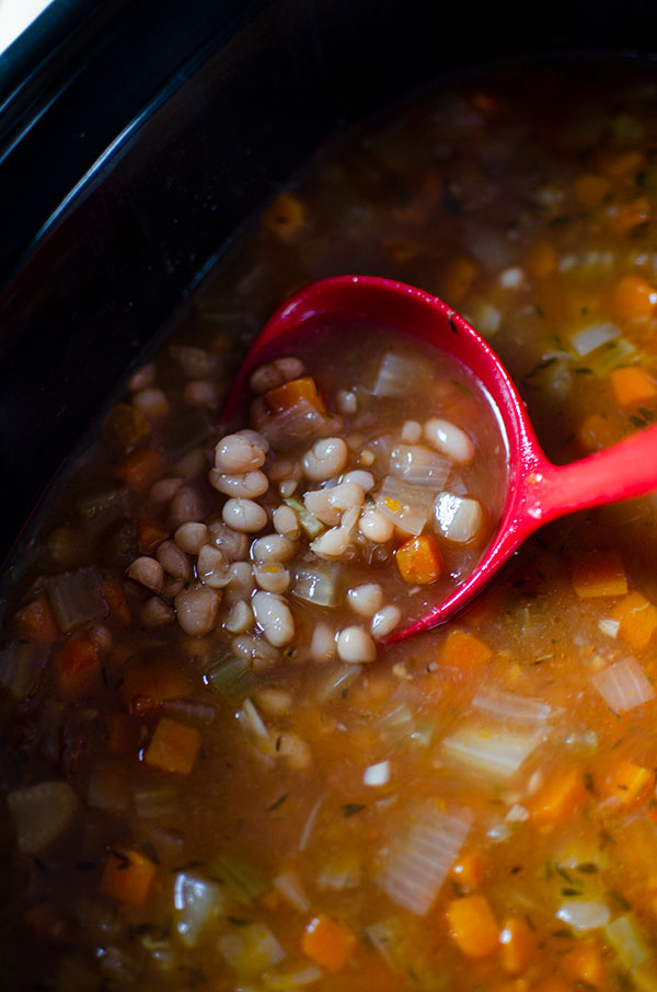 A ladle full of navy bean soup in the slow cooker.