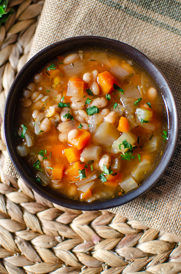 slow cooker navy bean soup in a black bowl with parsley on top