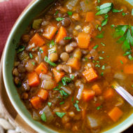 closeup of lentil soup in a green bowl with parsley sprinkled on top