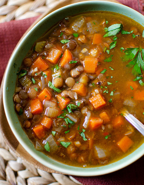 closeup of lentil soup in a green bowl with parsley sprinkled on top