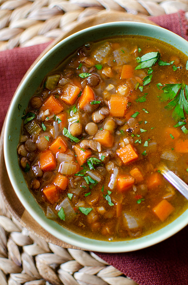 closeup of lentil soup in a green bowl with parsley sprinkled on top